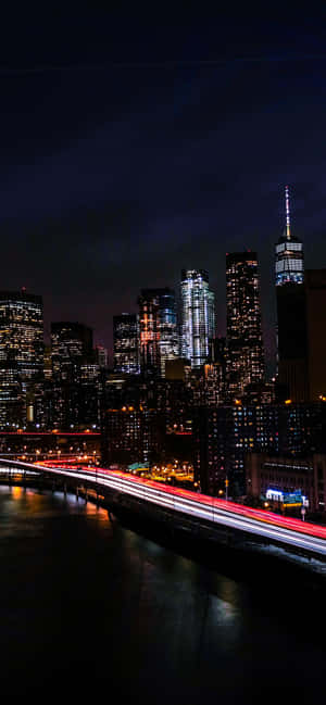 紐約天際線的夜景，建築物燈火通明，交通燈光形成光軌。 — Moto E 壁紙