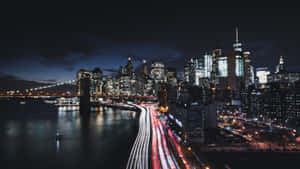 夜晚的城市景觀，橋附近有發光的摩天大樓和流動的交通燈光。 — 紐約市 壁紙