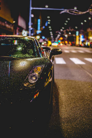 夜間濕漉漉的城市街道上停靠的黑色跑車，帶有模糊的燈光。