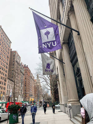 NYU旗幟掛在石建築上，城市街道上有行人經過。