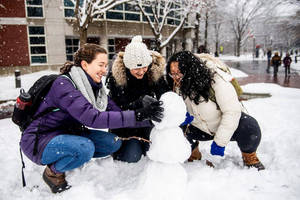 三位微笑的朋友在白雪覆蓋的校園庭院中堆雪人。