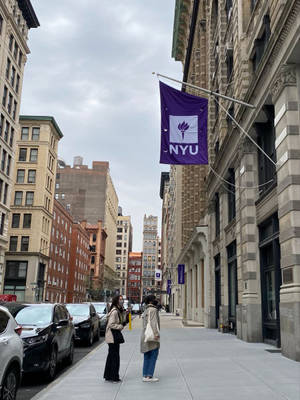 兩個人站在NYU旗幟下的行人路上。 — 紐約市 壁紙