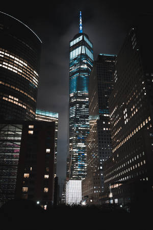 夜晚被藍色燈光照亮的高聳摩天大樓，位於其他城市建築之間。