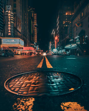 夜晚霓虹燈照亮城市街道，前景有沙井蓋。 — 夜晚 GIF 壁紙