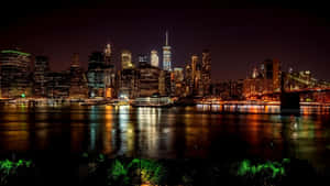 紐約天際線的夜景，有發光的建築物和水面上的橋樑。