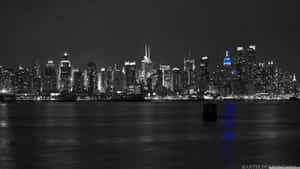 夜晚城市天際線景色，一座藍色發光的摩天大樓倒映在水中。