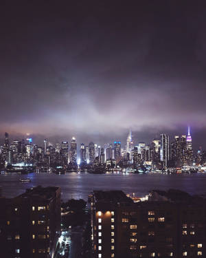 陰天之下，發光的摩天大樓與水面倒影的夜間城市景觀。