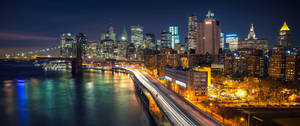 紐約天際線的夜景，有燈火通明的建築物和橋上車輛的光跡。