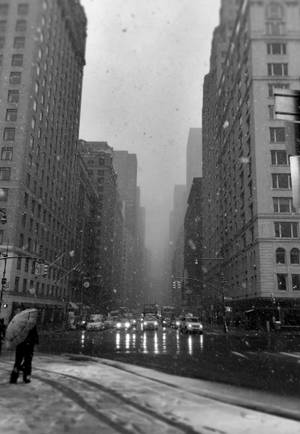 人在高樓之間的城市街道上撐傘在雪中行走。 — 雨天 壁紙