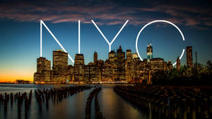黃昏時分的紐約市天際線，發光的NYC字母和寧靜的水面。