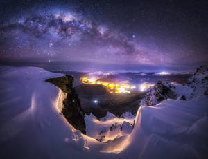 白雪覆蓋的山俯瞰著一個在星空和銀河下的明亮山谷。
