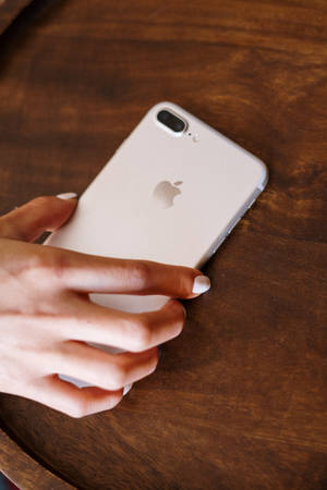 一隻手在木質表面上拿著一部銀色iPhone。