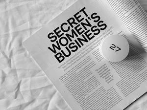 一篇標題為 Secret Women's Business 的雜誌文章放在白色布料上，帶有顯示 27 的頁碼標記。 — 純白色 壁紙