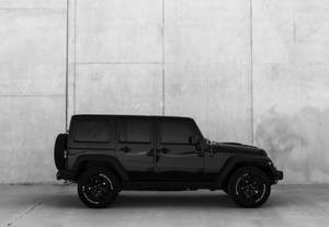 黑色Jeep Wrangler停在混凝土牆前的黑白照片。