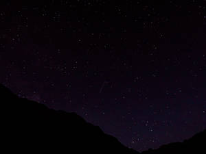 流星越過山脈剪影，在星空夜空下