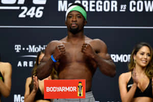 赤裸上身的MMA拳手在UFC稱重活動中自信地擺姿勢，戴著綠色頭帶和贊助商標誌。