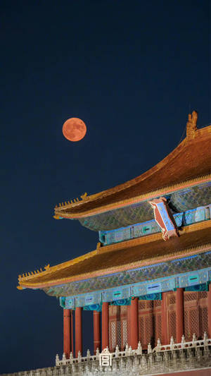 一輪橙色滿月在夜間升起在傳統中國宮殿屋頂上方。