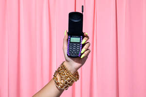 手帶有亮黃色指甲和金色鏈條手鐲，拿著一部黑色翻蓋手機。 — Motorola 壁紙