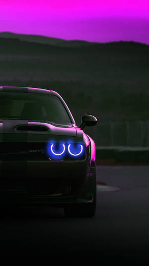黑色道奇挑戰者SRT Hellcat，帶有發光的藍色頭燈，在黃昏時分的賽車場上。