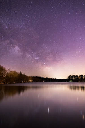 結冰的湖面反射出帶有銀河和森林剪影的星空紫色夜空。