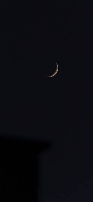 一彎月牙在黑暗的夜空中閃耀，位於建築物剪影之上。