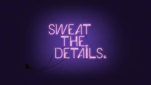 深色牆壁上寫著「SWEAT THE DETAILS」的紫色霓虹燈牌。