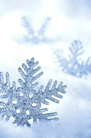 一顆閃亮的銀色雪花躺在雪地上，後面有模糊的雪花。 — 雪 壁紙