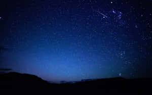 一顆流星劃過繁星點點的夜空，上方是黑暗的山巒輪廓。 — 夜空 壁紙