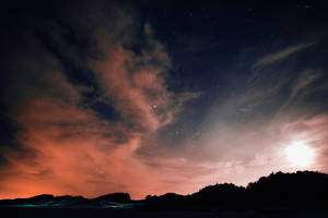 繁星點點的夜空，橙雲和月亮，在黑暗的山丘上方。