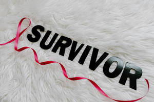 黑色 'SURVIVOR' 字母配紅色絲帶，背景為白色絨毛。 — 粉紅 壁紙