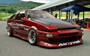 賽車場上的紅色改裝豐田AE86飄移車，背景有綠色山丘。