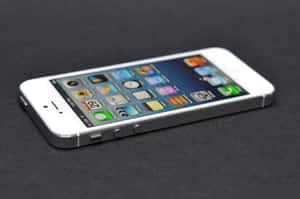 白色 iPhone 5s 螢幕上顯示色彩繽紛的應用程式圖標，放置在深色表面上 — 美學 iPhone 壁紙