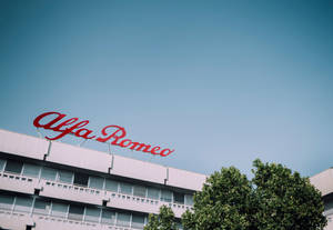 現代建築頂部的 Alfa Romeo 標誌，伴隨著樹木和藍天。