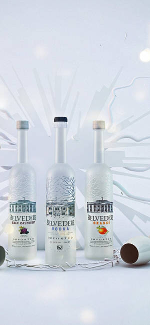 三瓶Belvedere伏特加酒，標籤顯示口味，排列在白色表面上，帶有抽象燈光效果。 — iPhone Air 壁紙