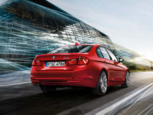 紅色BMW 320i房車在日落時分飛馳穿過現代玻璃建築。