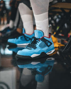 淺藍色 Jordan 4 運動鞋，帶有黑色點綴和白色襪子，位於反光的籃球場上。