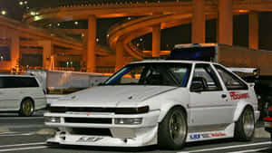 夜間停放在照明高速公路高架橋下的白色AE86賽車。
