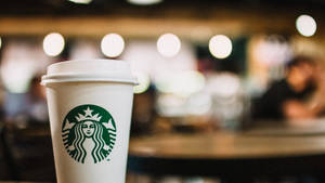 在舒適的咖啡館中，一個Starbucks咖啡杯，背後有柔和模糊的燈光。