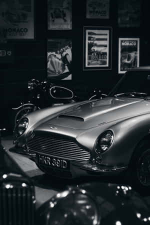 銀色經典 Aston Martin DB5 在博物館中展示，配有賽車海報。 — 小米Pad 9 Pro Max 壁紙