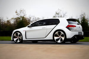 白色Volkswagen Golf GTI Concept在秋樹間的道路上飛馳。