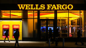 人們夜晚經過帶有黃色標誌的 Wells Fargo 銀行。