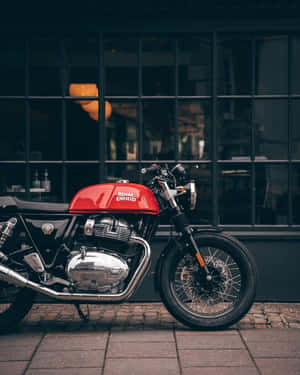 紅色 Royal Enfield 電單車夜間停泊在鵝卵石街道上，靠近玻璃建築。