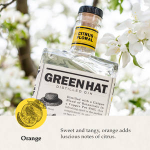 一瓶 Green Hat Citrus Floral 氈酒被白色花朵包圍，帶有橙色柑橘圖案。