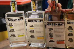 四瓶 Green Hat 氈酒，標籤上有帽子設計，其中一瓶由一隻手拿著。