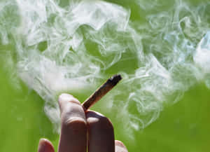 手拿著點燃的大麻煙，煙霧在綠色背景上升起