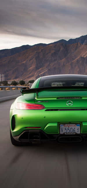 綠色 Mercedes-AMG GT R 在沙漠公路上疾馳，山脈在後。 — Galaxy M06 壁紙