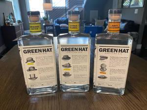 三瓶 Green Hat 氈酒，帶有不同風味標籤，放在木桌上。