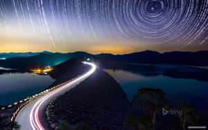 星軌在蜿蜒的道路上空盤旋，黃昏時水壩附近有汽車的光跡。