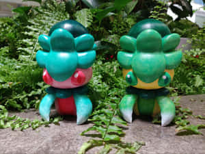 兩個上色嘅 Bulbasaur 公仔喺石頭表面嘅蕨類植物之間。 — 卡通 壁紙