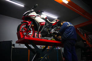 機械師在車庫的升降台上維修一輛紅白相間的Yamaha電單車。